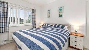 A bedroom with a large bed, a nightstand with a lamp, and two framed pictures on the wall. - Kittiwake - Short Walk to Beach and Village (Saundersfoot)