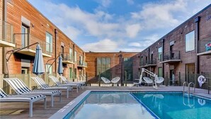 Un espace piscine doté de chaises longues et de parasols, entouré d’immeubles en briques avec des balcons.