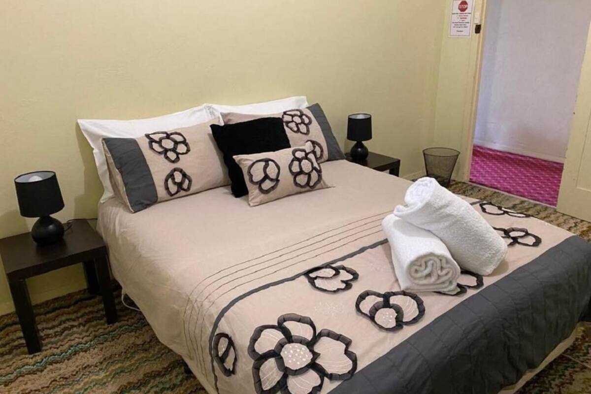 Ein ordentlich bezogenes Bett mit einem blumigen Überwurf, zwei Nachttischlampen und ein gefaltetes Handtuch auf dem Bett.