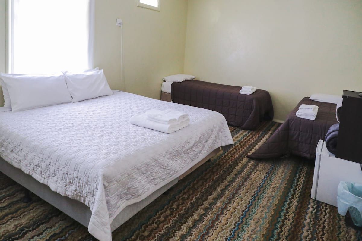 Ein Hotelzimmer mit einem großen Bett, zwei Einzelbetten, einem kleinen Schreibtisch und einem Mülleimer.