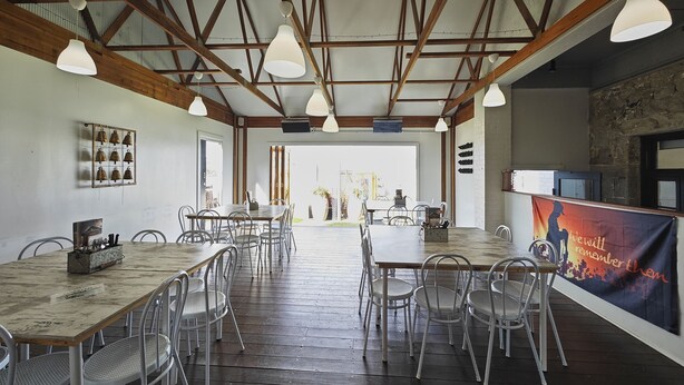 A spacious dining area with wooden tables and metal chairs, a high ceiling with exposed beams, and a banner with a message. - Royal Hotel Capertee (Capertee)