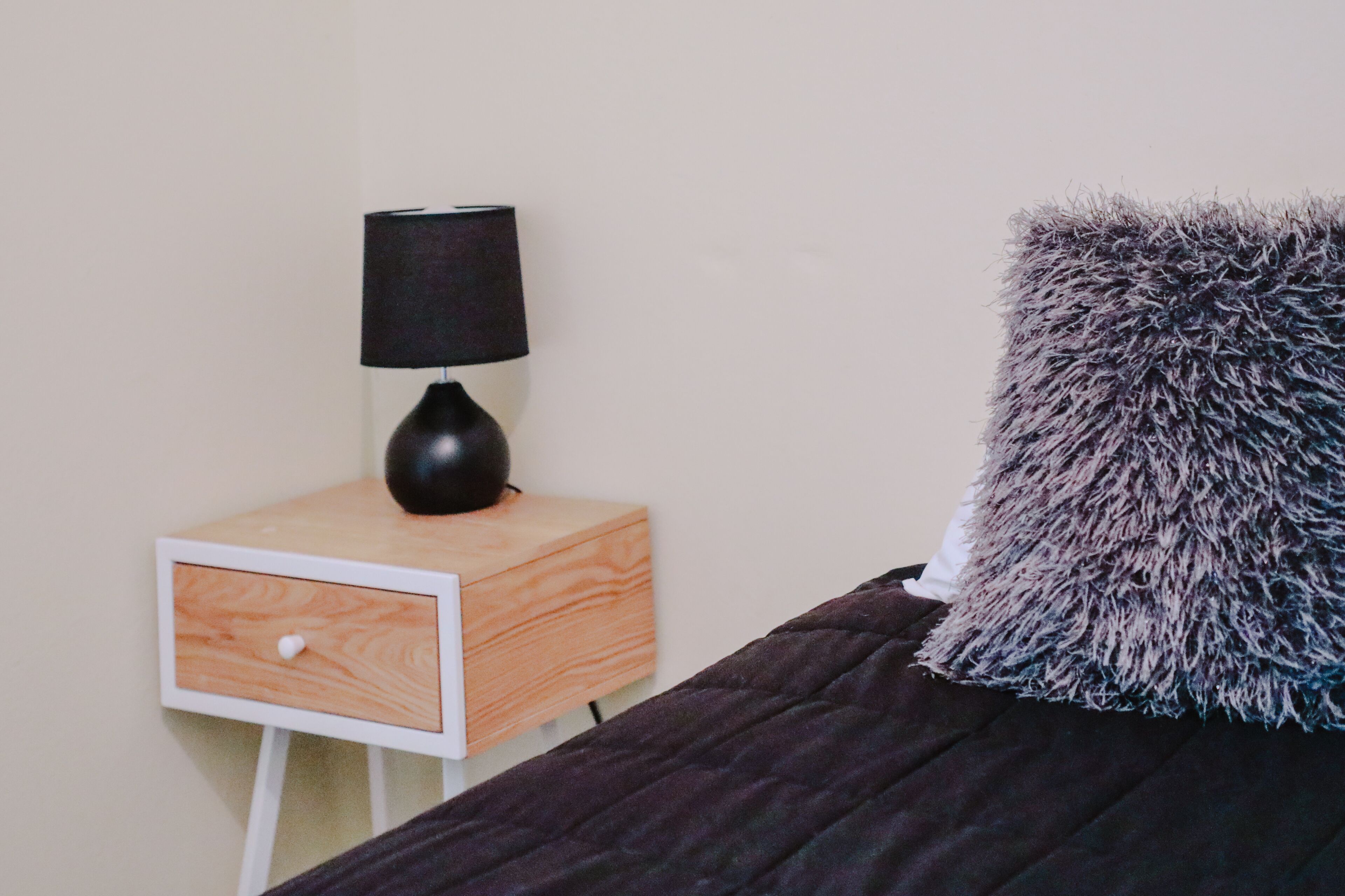 A bedroom with a bed, a nightstand with a lamp, and a pillow.