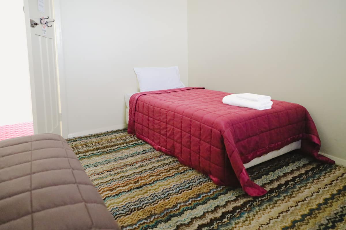 Ein Schlafzimmer mit einem Bett, einem weißen Kopfkissen, einer roten Tagesdecke und einem Streifenmuster-Teppich.