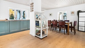 A modern kitchen with teal cabinets, a white island, and a dining area with wooden chairs and a table. - "Alica" - 200m from the sea by Interhome (Nexø)