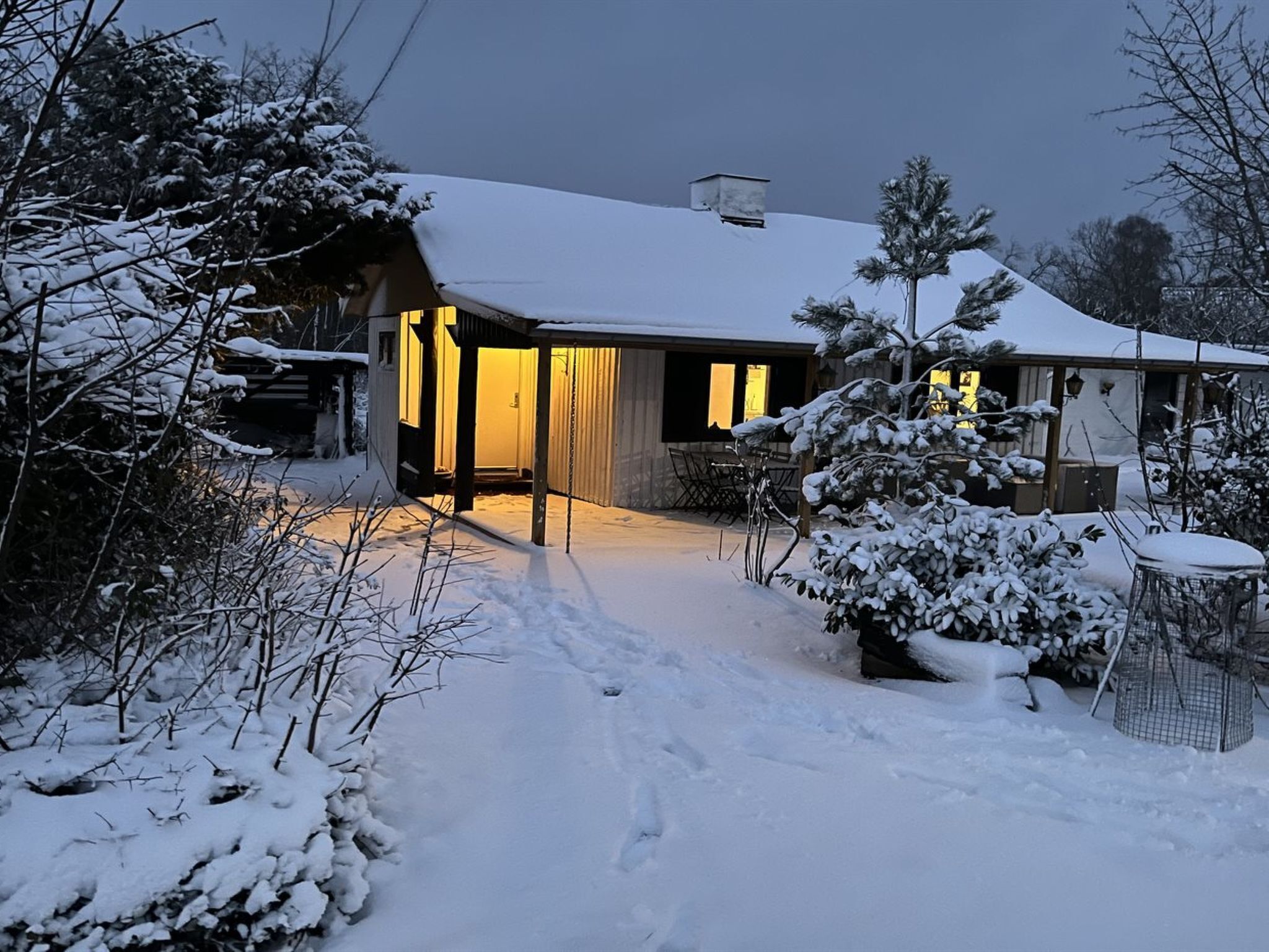 A snow-covered house with a visible garage and a covered outdoor seating area.
