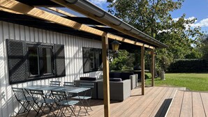 A covered outdoor patio with a wooden deck, metal-framed tables and chairs, and outdoor lighting fixtures. - "Alica" - 200m from the sea by Interhome (Nexø)