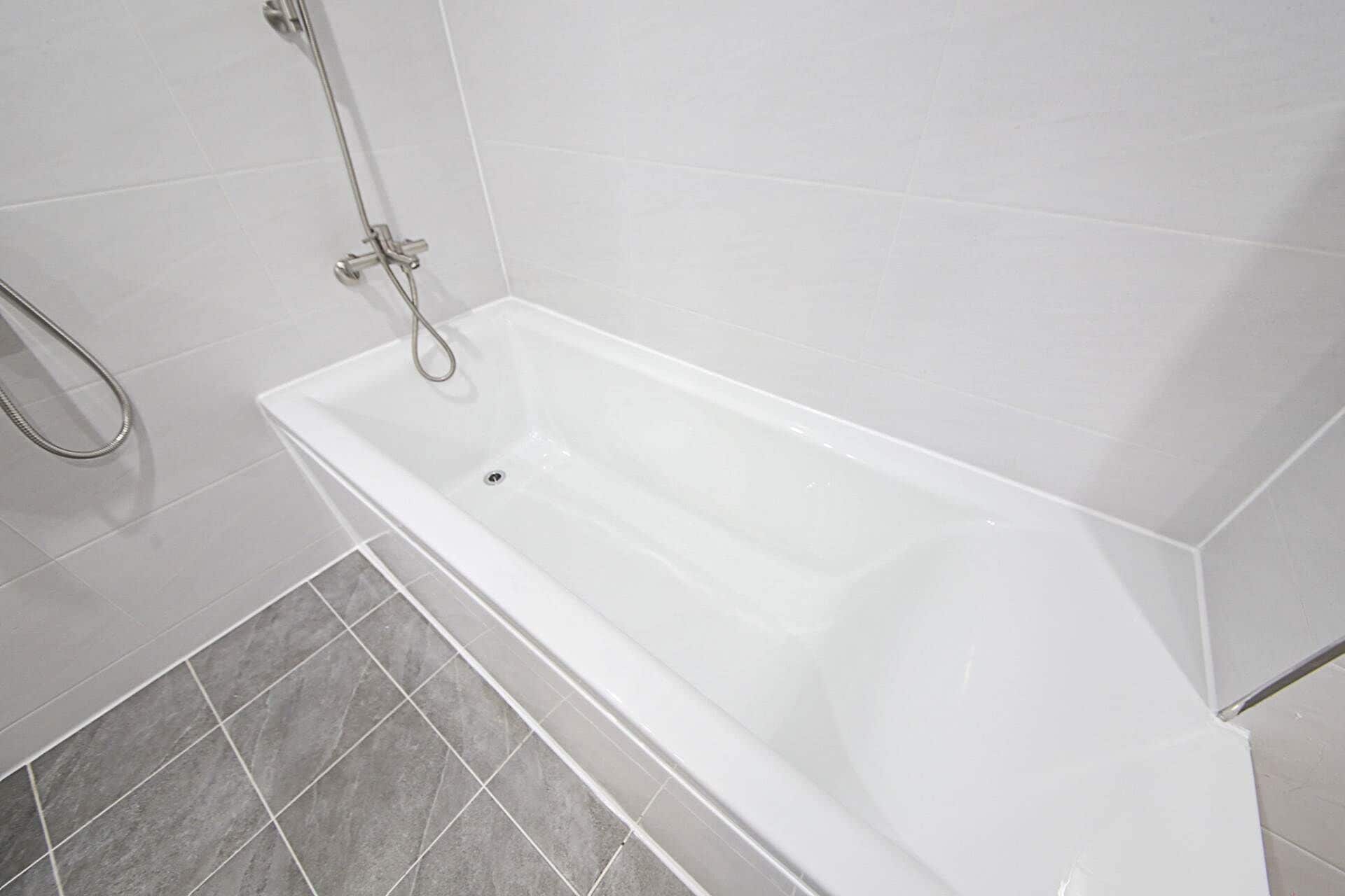 A bathtub with a shower head and a drain, set in a bathroom with grey tiles.