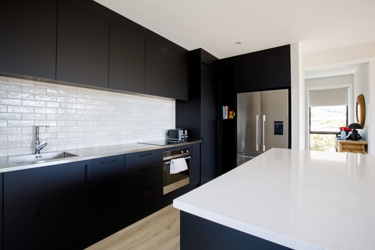 A modern kitchen with black cabinets, a white countertop, and stainless steel appliances.