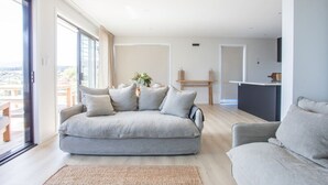 A modern living room with a grey sofa, a smaller armchair, and a coffee table. There is a large window providing a view of the outdoors. - Super Central in Wanaka - Luxury villa only a 10 minute walk to town (Wanaka)