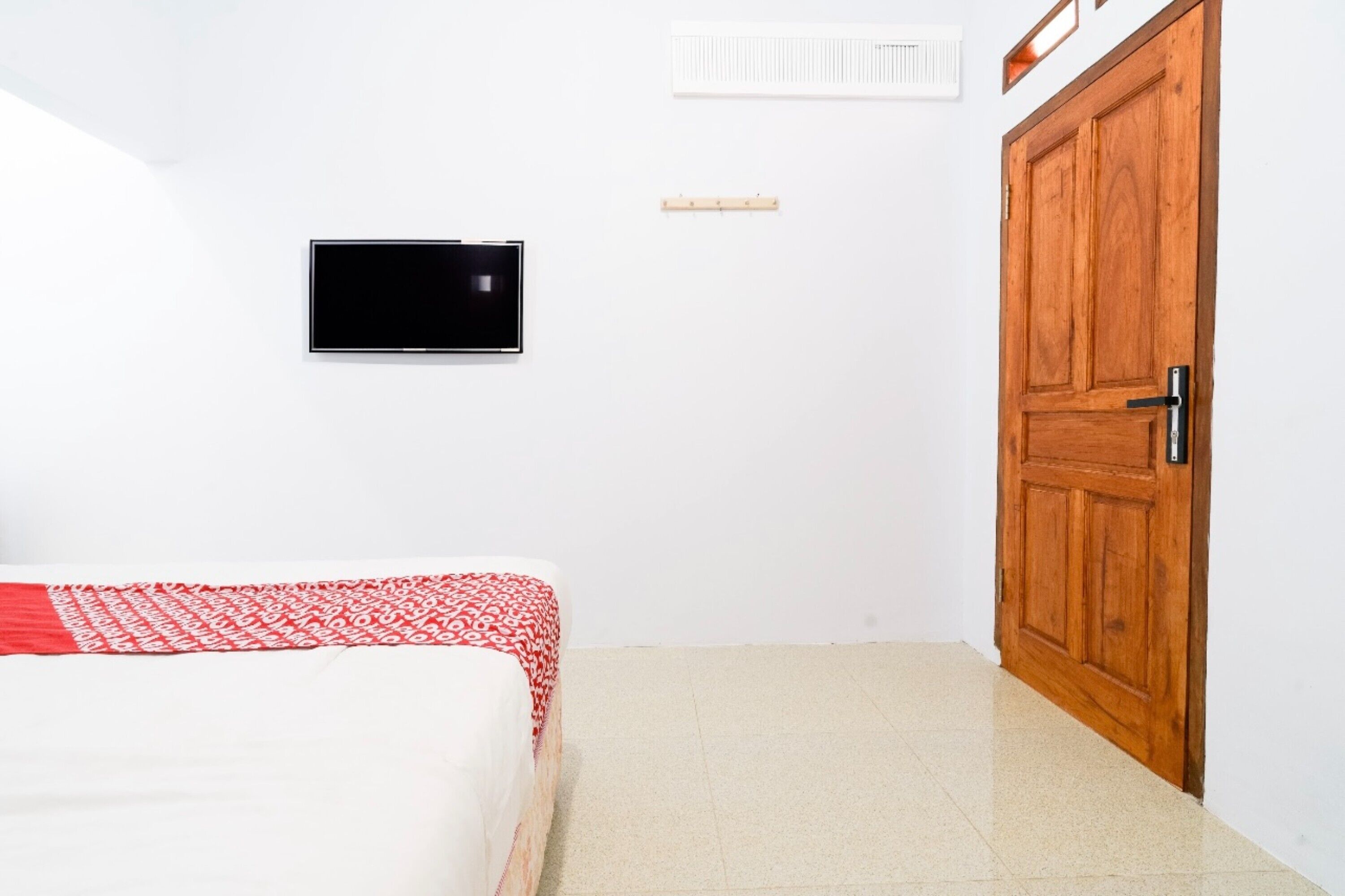Un dormitorio con cama, televisión en la pared, puerta de madera y pared blanca.