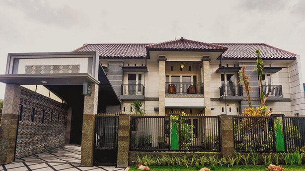 A two-story house with a tiled roof, a gated entrance, and a landscaped garden.