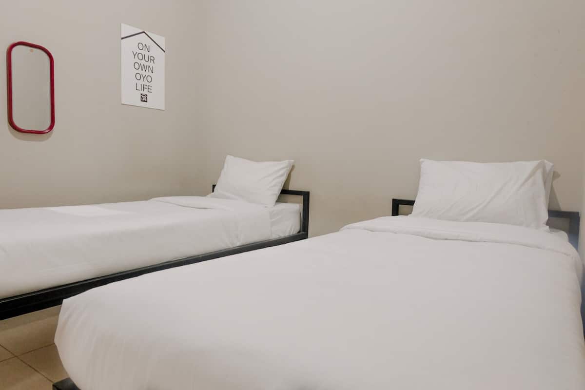 Zwei Einzelbetten mit weißen Laken in einem Zimmer mit schlichter Wand und einem Schild, auf dem 'ON YOUR OWN OYO LIFE' steht.