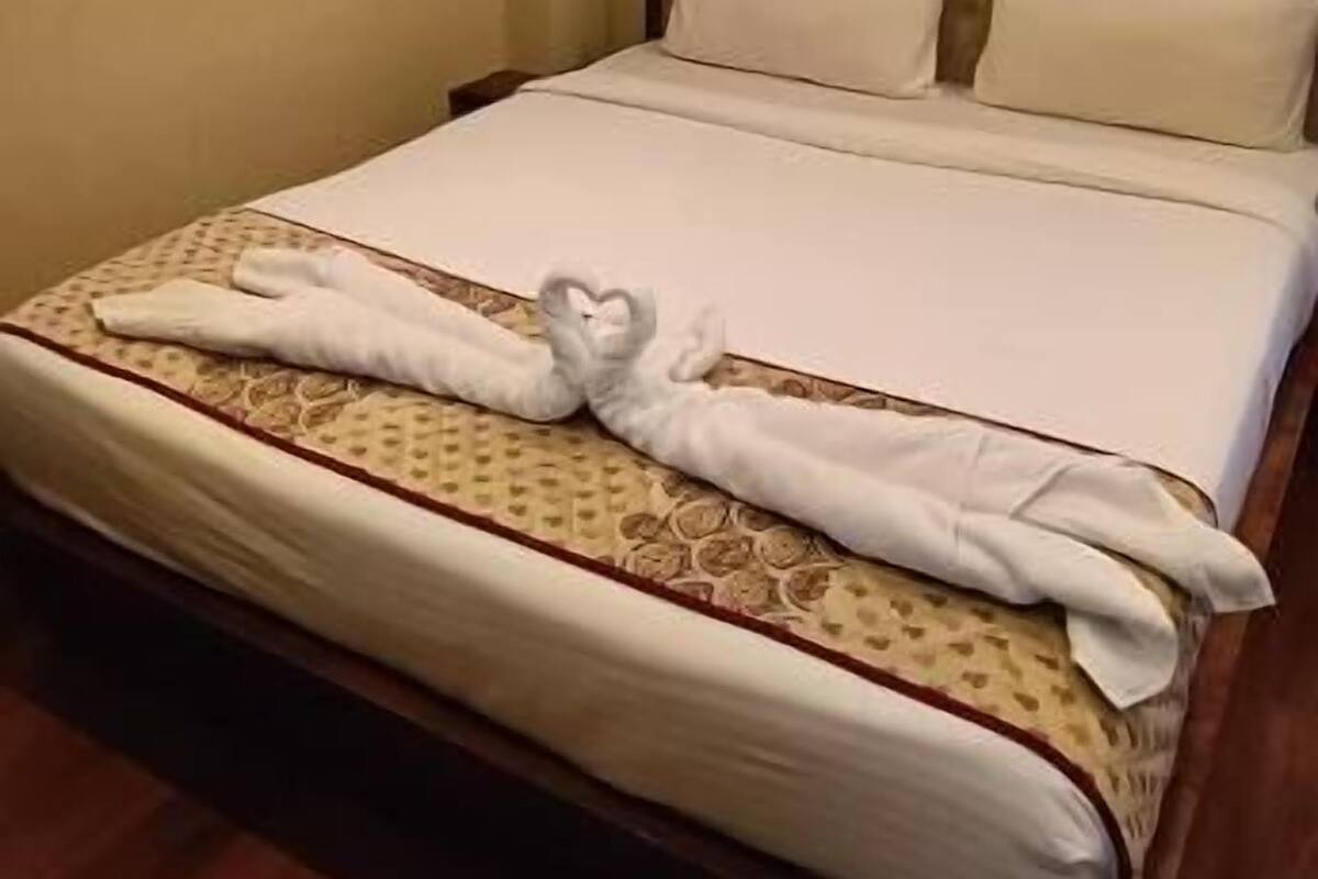 A neatly made bed with a heart-shaped towel, a wooden headboard, and a wooden floor.