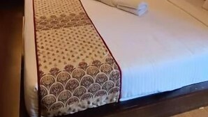 A neatly made bed with a patterned bedspread, a window with curtains, and a wooden floor. - Hotel A One Luxury (Puri)