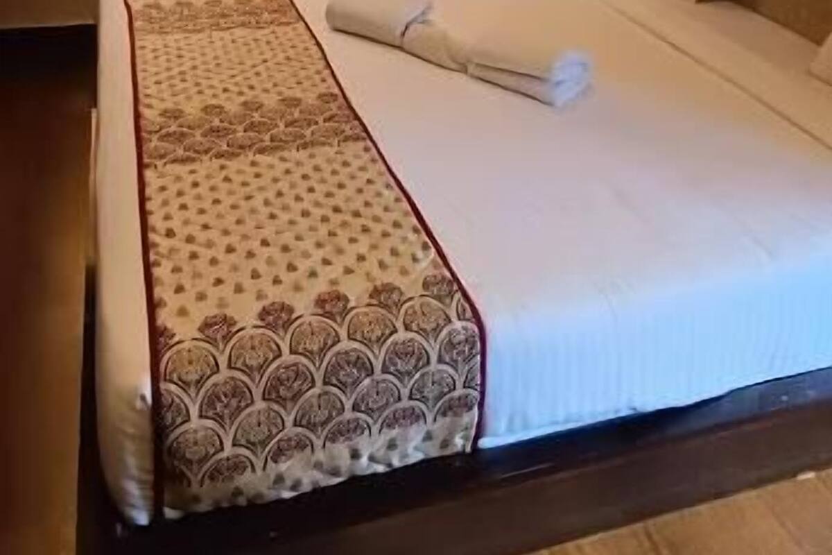 A neatly made bed with a patterned bedspread, a window with curtains, and a wooden floor.