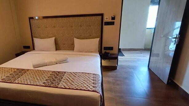 A neatly made bed with a patterned bedspread, a headboard, and a bedside table with a lamp. - Hotel A One Luxury (Puri)
