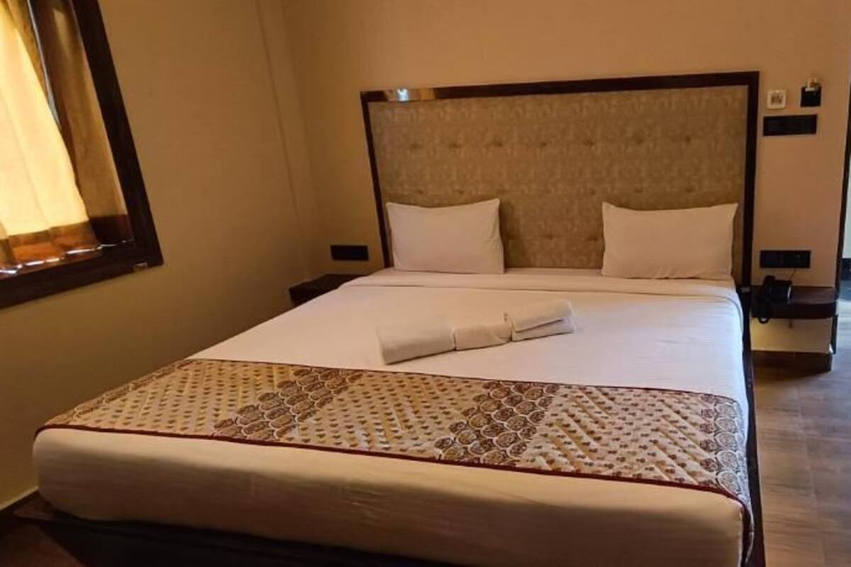A neatly made bed with a patterned bedspread, a headboard, and a bedside table with a lamp.