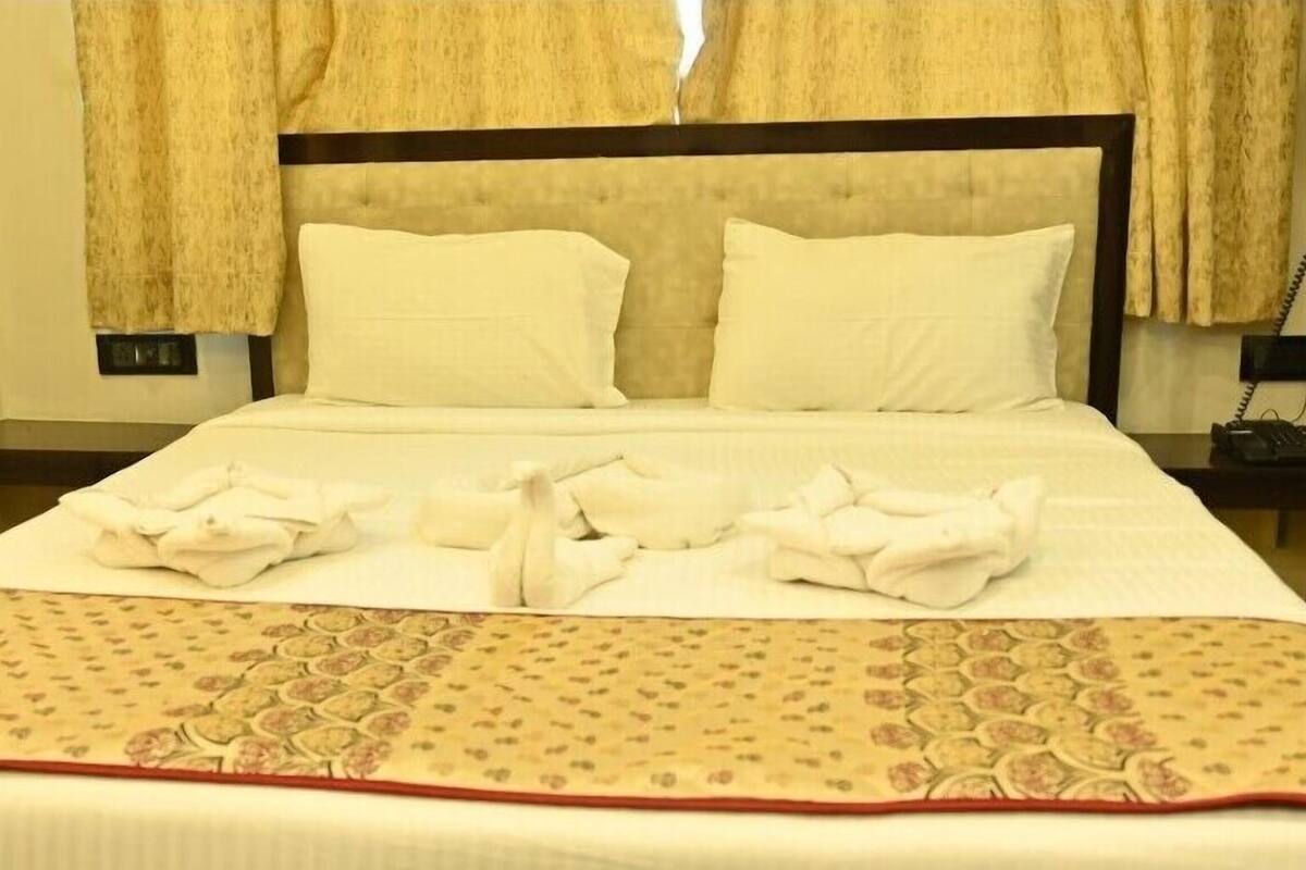 A neatly made bed with a patterned throw blanket and pillows, a bedside telephone, and a nightstand with a lamp.