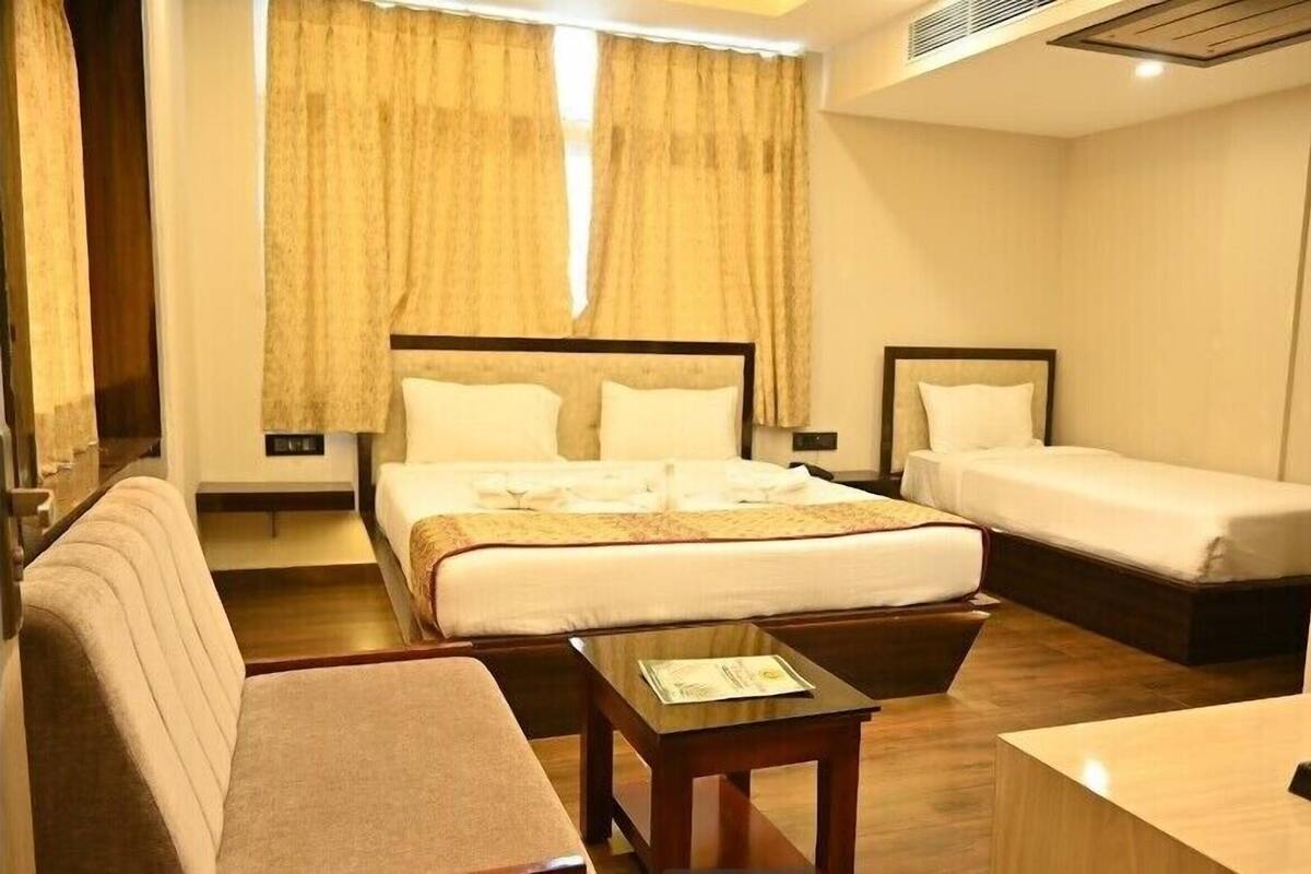A hotel room with a large bed, a smaller bed, a sofa, a desk, and a mirror.