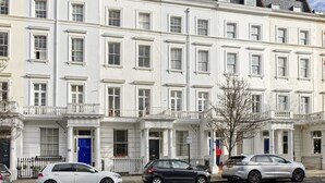 A row of white townhouses with uniform window designs and a central entrance. - Spacious Pimlico Apartment by Underthedoormat (London)