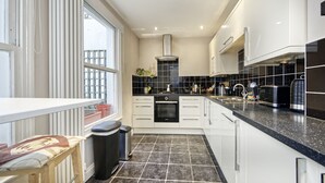 A modern kitchen with white cabinets, a black countertop, and a tiled backsplash. - Spacious Pimlico Apartment by Underthedoormat (London)