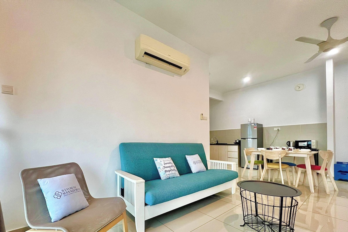 Una sala de estar con sofá, sillón, una mesita y una kitchenette al fondo.