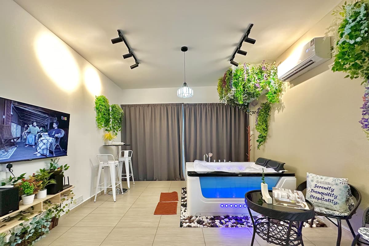 Una habitación de hotel moderna con televisor, camilla de masaje, una pequeña zona de comedor y un ventanal con cortinas.