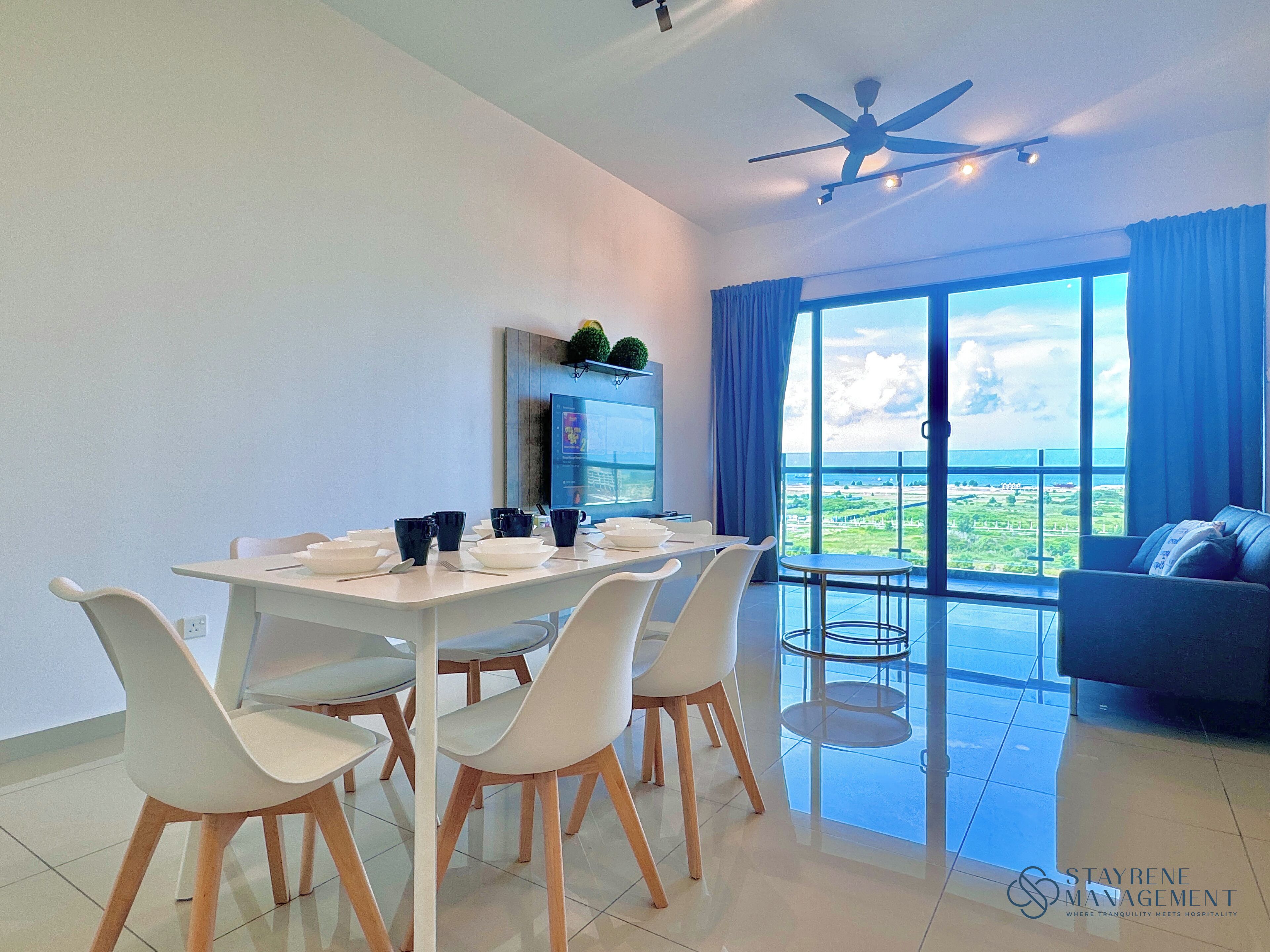 A modern dining area with a table set for four, white chairs, and a view of the sea through large windows.