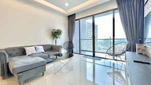A modern living room with a sofa, two chairs, a small table, a potted plant, and a large window with curtains. - Atlantis Residences Melaka by Stayrene (Malacca City)