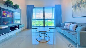 A modern living room with a flat-screen TV, a sofa, a coffee table, and a large window offering a view of the landscape. - Atlantis Residences Melaka by Stayrene (Malacca City)