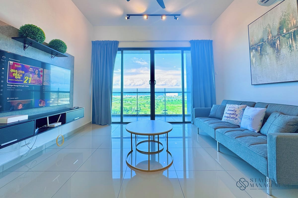 Una sala de estar moderna con televisor de pantalla plana, un sofá, una mesa de centro y un amplio ventanal con vistas al paisaje.