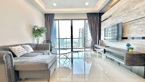 A modern living room with a grey sofa, a glass coffee table, and a TV mounted on the wall. - Atlantis Residences Melaka by Stayrene (Malacca City)