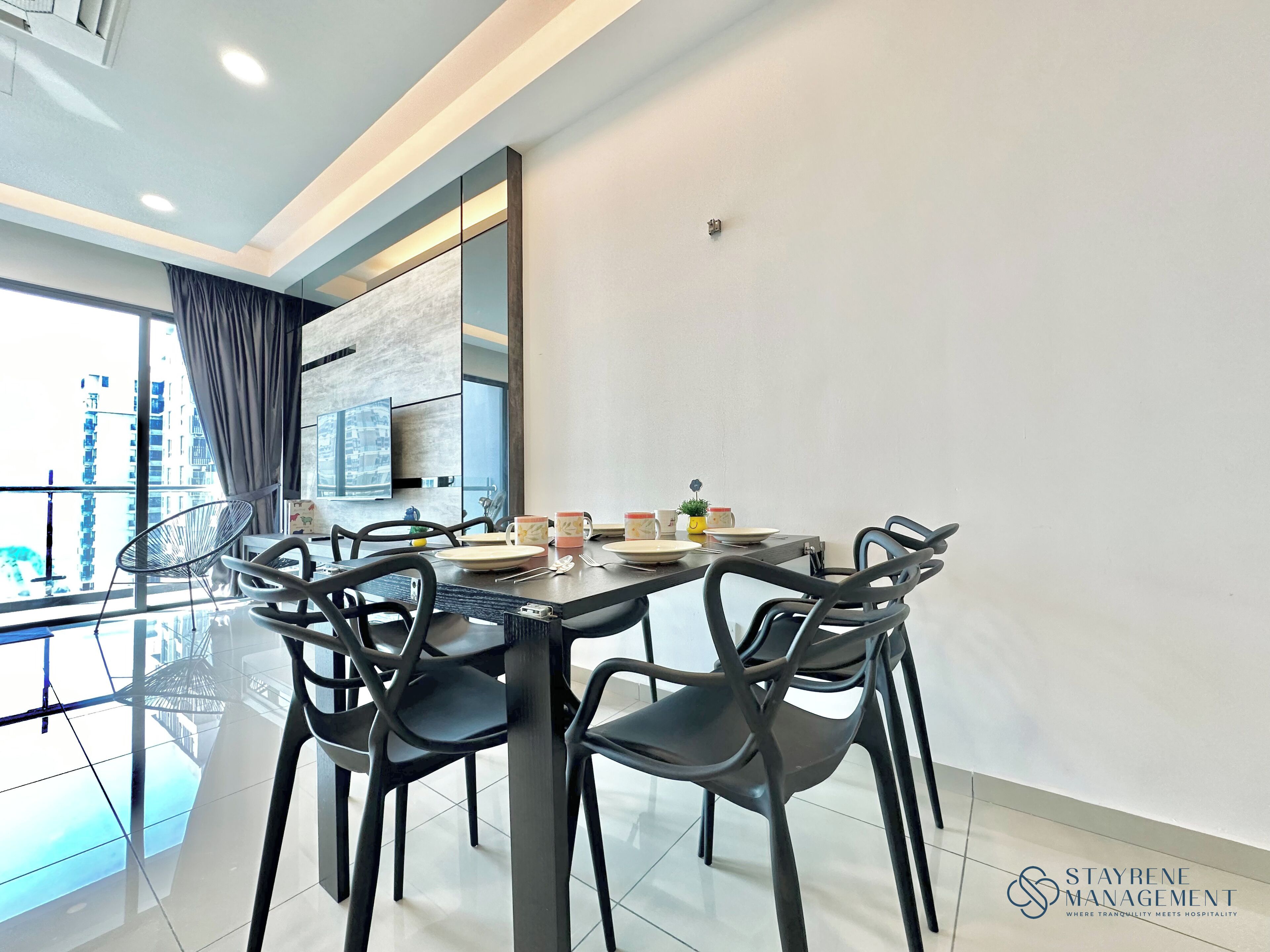 A modern dining area with a glass table, black chairs, and a view of the city through large windows.