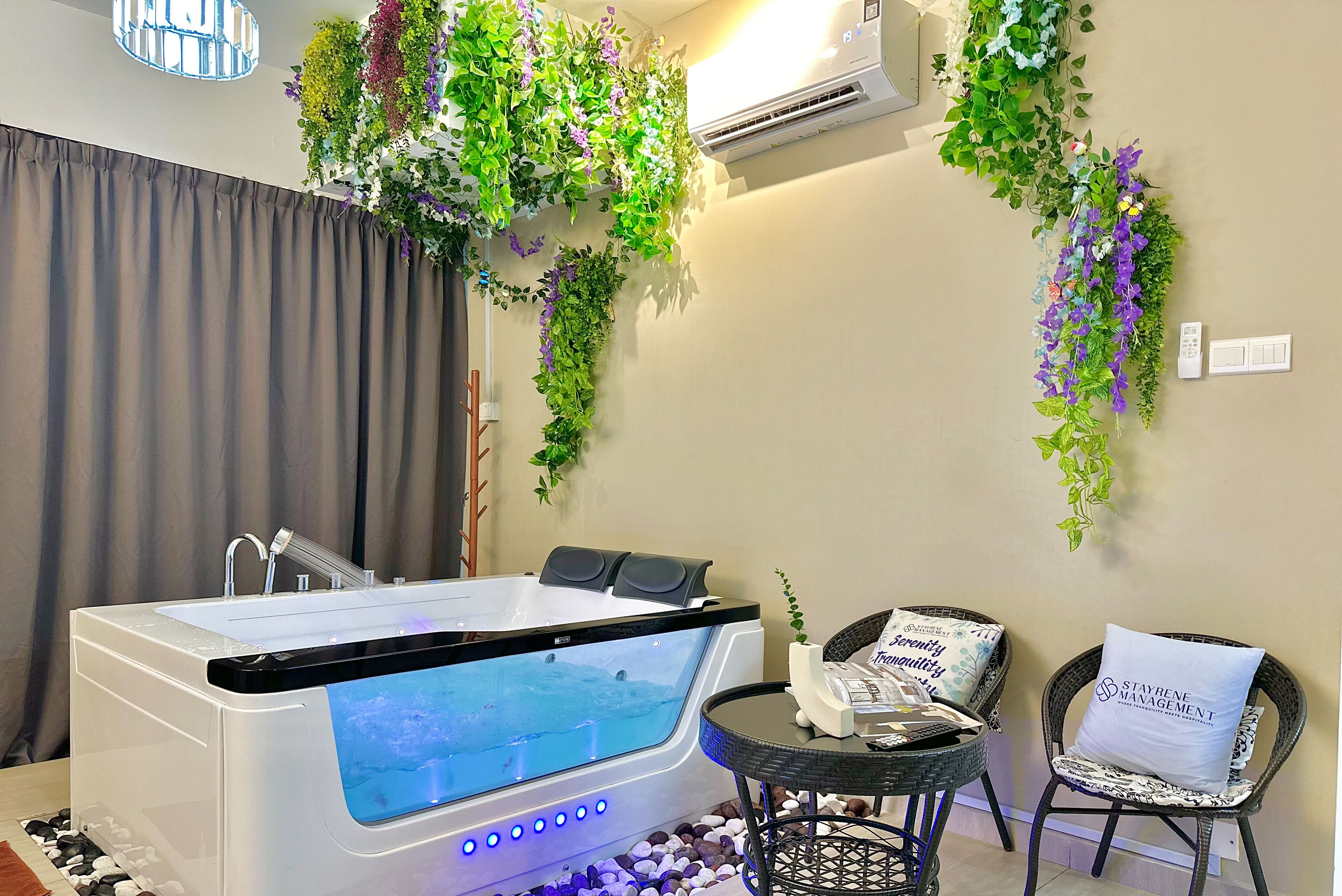 A modern spa room with a large bathtub, a small table with magazines, and decorative plants on the walls.