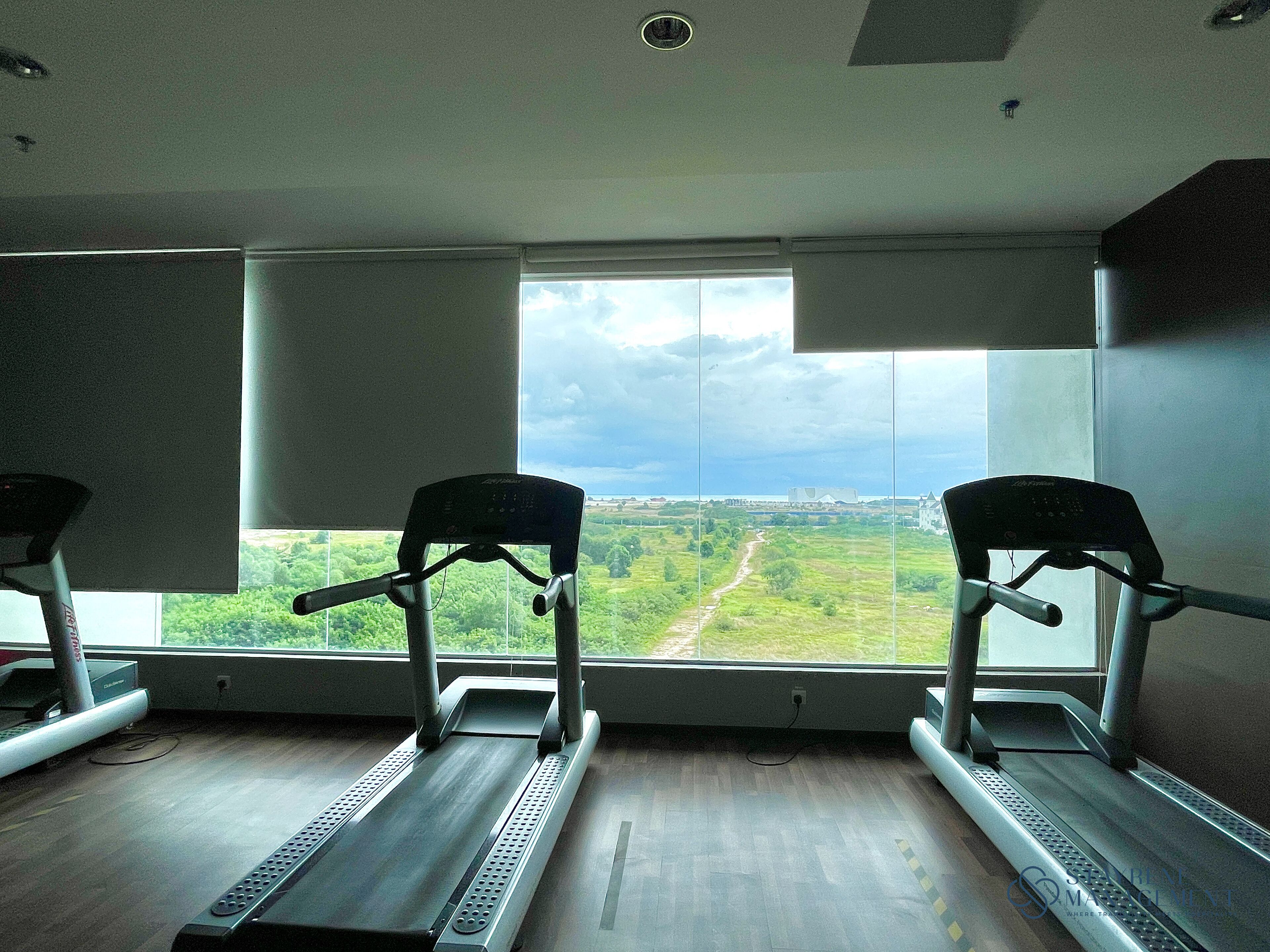 Une salle de sport équipée de tapis de course et dotée d’une grande fenêtre donnant sur un paysage verdoyant.