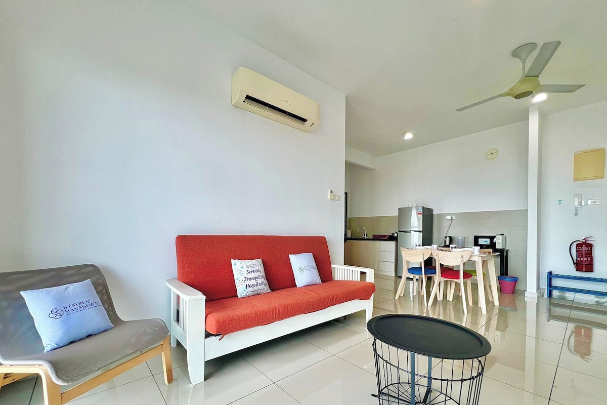 Una sala de estar moderna con un sofá rojo, un sillón gris, una mesita redonda y un ventilador de techo.
