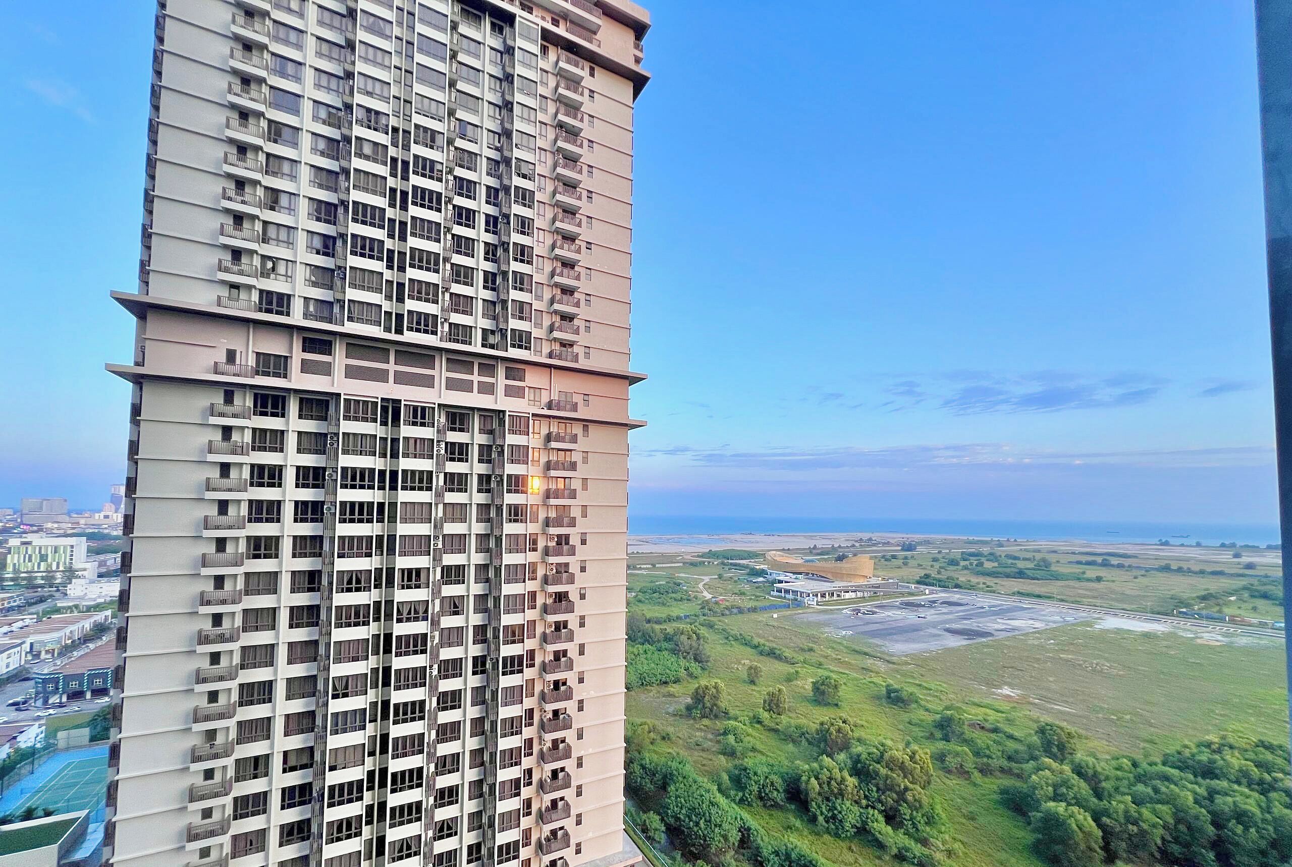 Um edifício alto com várias varandas e vista para uma paisagem verde e a costa distante.