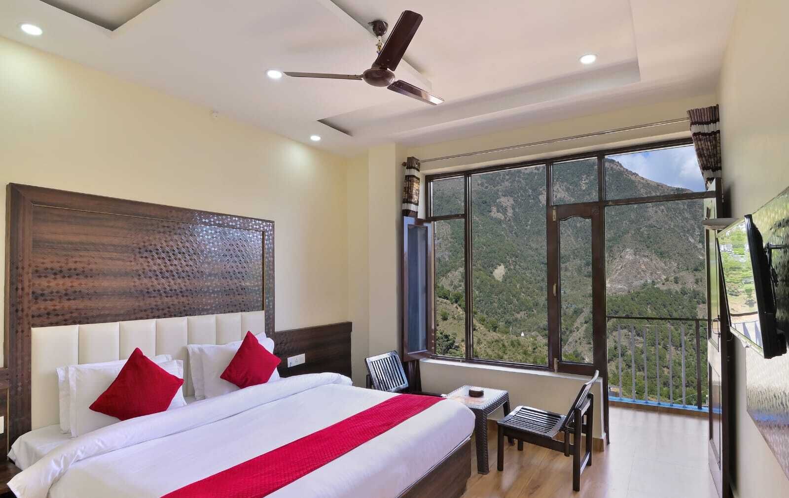 A hotel room with a large bed, a ceiling fan, a window with a mountain view, and a TV mounted on the wall.