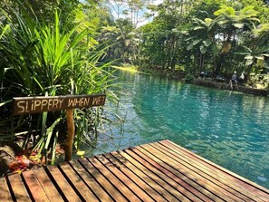 A wooden deck by a clear blue pool with a sign warning of slipperiness when wet. - Exclusive Sunrise Eco Resort (Saraotou)