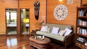 Una habitación acogedora con piso de madera, un sofá verde, una mesita de centro de mimbre y una estantería llena de libros.