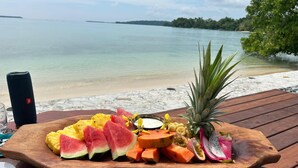 Una tabla de madera con varias frutas y una piña sobre una mesa en la playa.