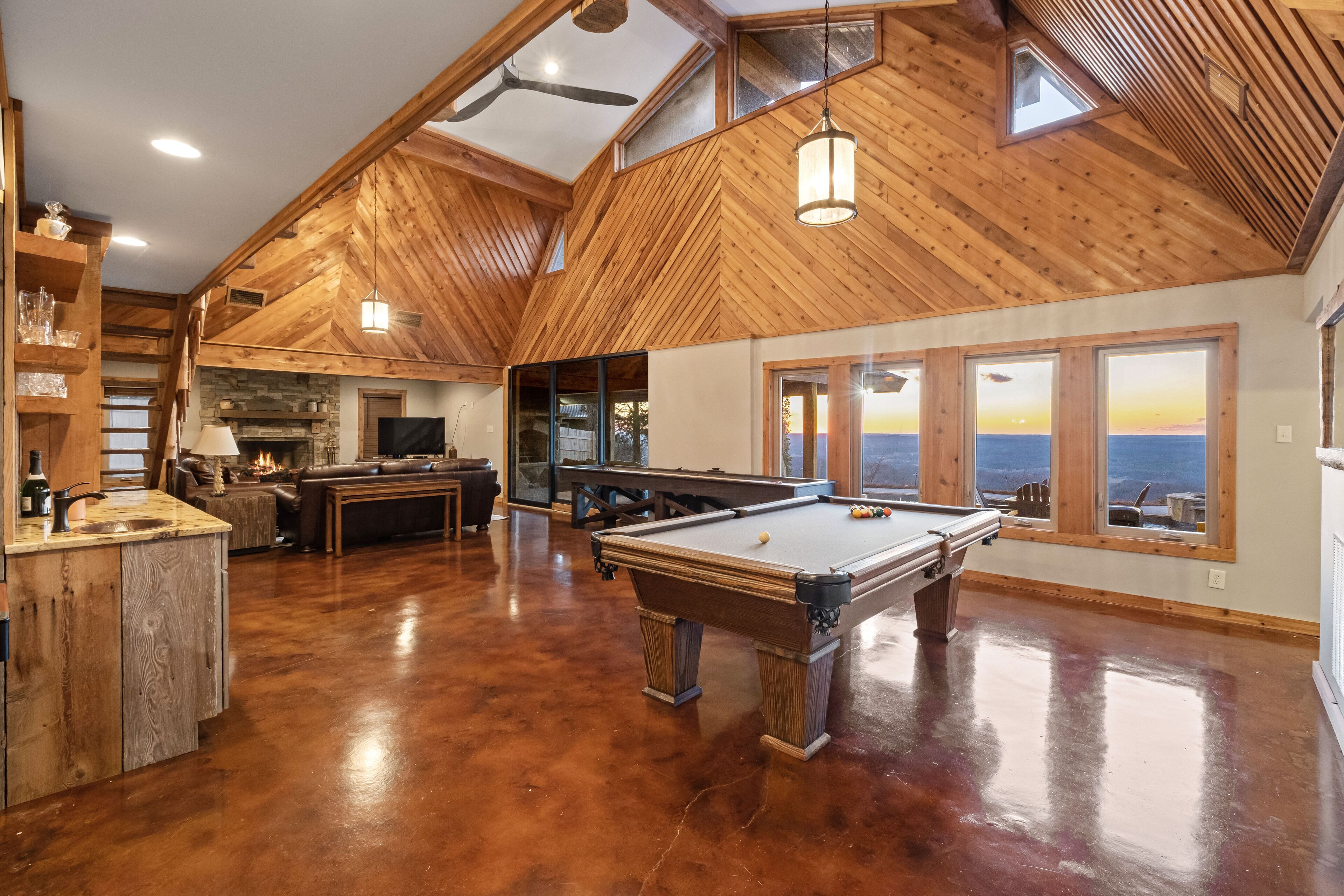 A spacious room with a pool table, wooden ceiling, and large windows offering a view of the ocean.
