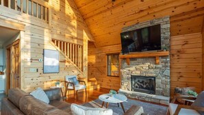 L’intérieur chaleureux d’un chalet avec une cheminée en pierre, des murs en bois, un canapé et un téléviseur fixé au-dessus de la cheminée.