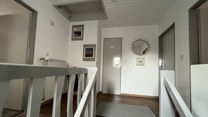Een gang met een houten vloer, witte muren en een deur met een spiegel erboven.