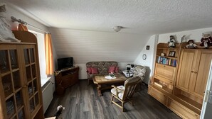 Een gezellige woonkamer met een bank, fauteuils, een houten kast en een televisie.