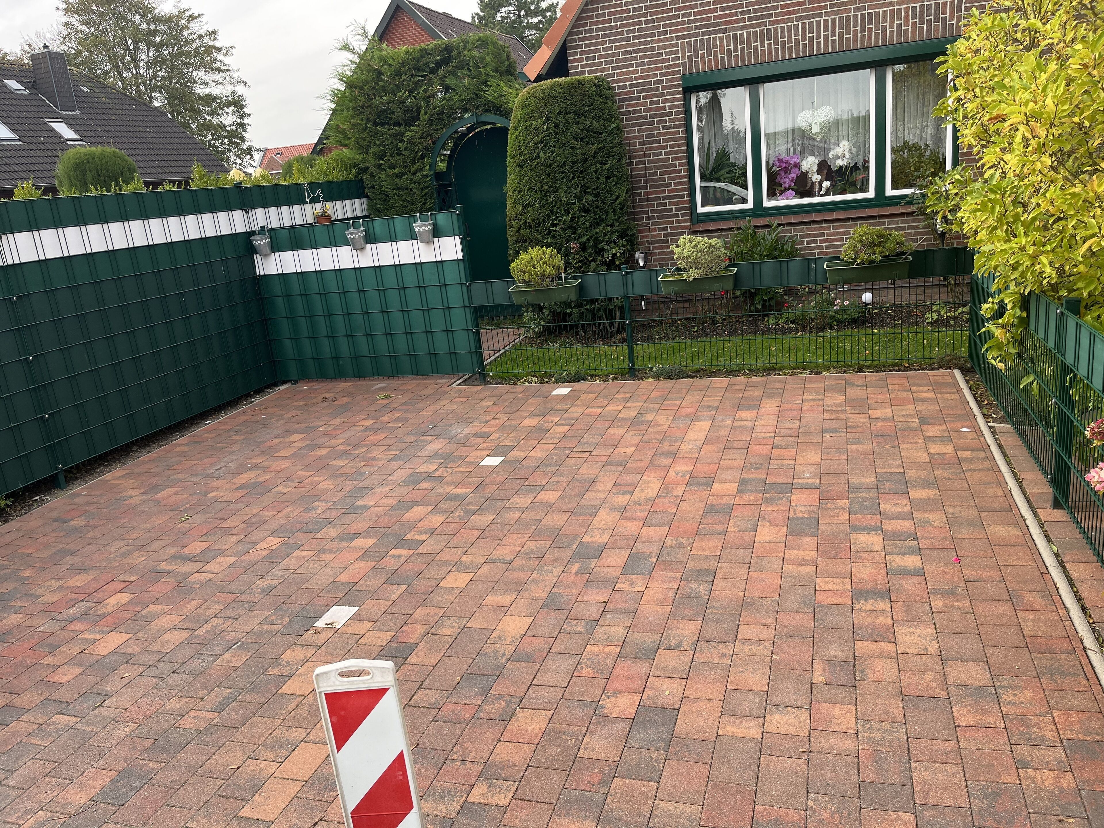 Un patio empedrado con diseño de ladrillo, rodeado por una cerca verde y un muro de ladrillo.