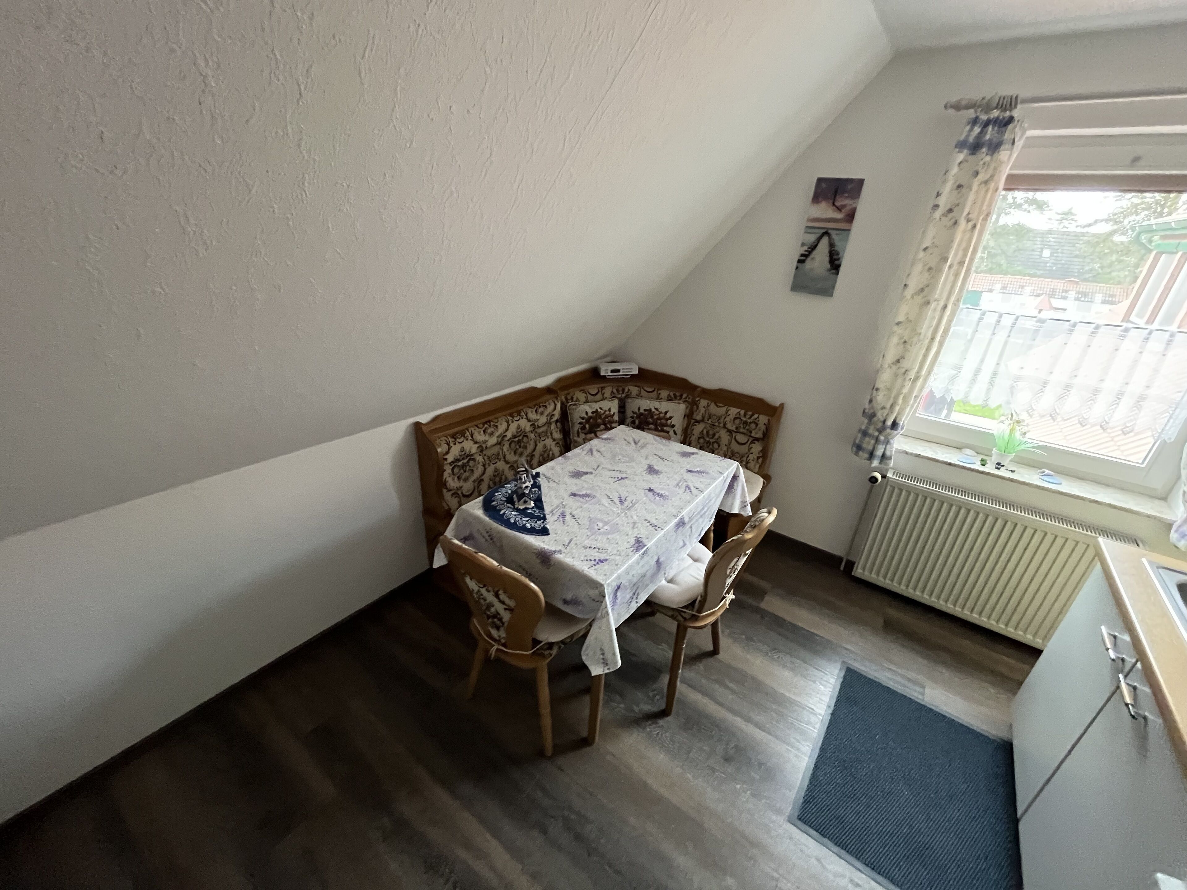 Ett litet, ombonat rum med ett träbord och stolar, ett element och ett fönster med gardiner.