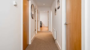 A narrow hallway with wooden doors on both sides, a radiator on the right, and a mirror on the left. - Stunning 3BD Flat, Parking, Sleeps Six, Near Park (London)