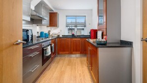 A modern kitchen with wooden cabinets, stainless steel appliances, and a large window providing natural light. - Stunning 3BD Flat, Parking, Sleeps Six, Near Park (London)