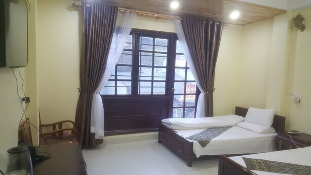 A bedroom with a single bed, a wooden headboard, a small table, and a window with curtains.